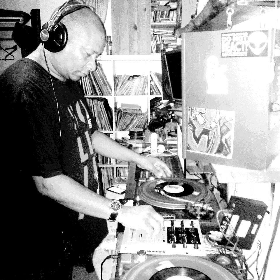 Tony Tee playing records on turntables for Codesouth Radio reggae 7 inch vinyl standing up for cancer